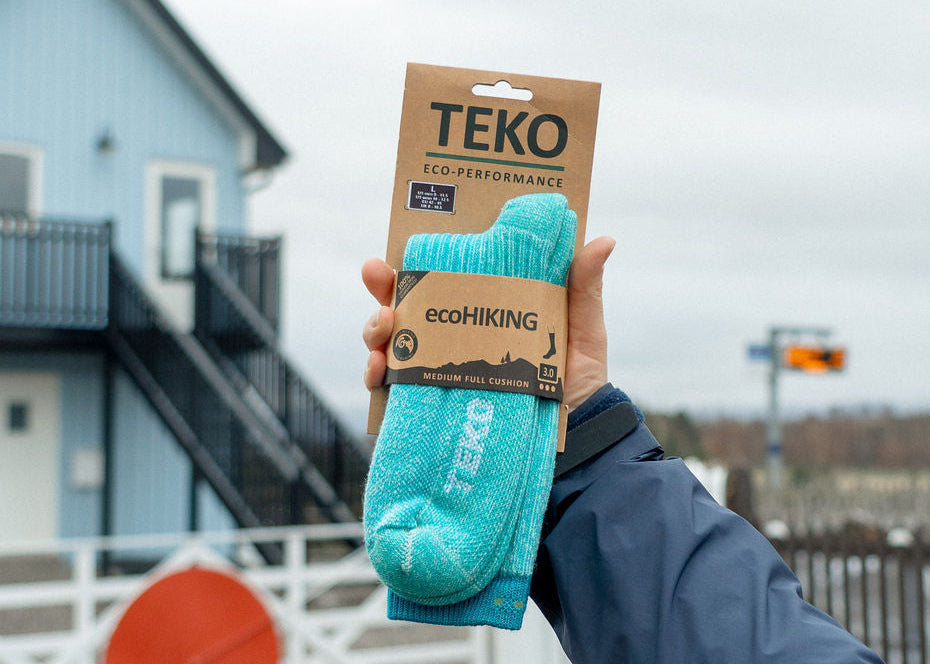 Turquoise sock held in front of a building with a cloudy sky