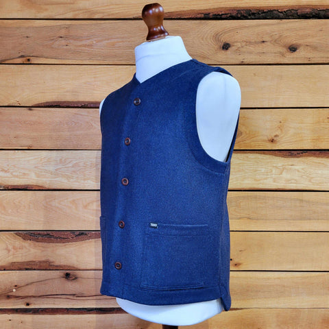 A blue unisex waistcoat made of recycled wool, displayed on a mannequin against a wooden backdrop.