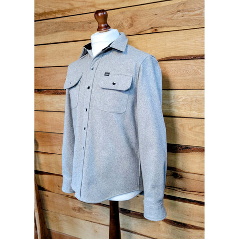 A men's long-sleeved shirt with two chest pockets, button-secure flaps, collar, and sleeve plackets, displayed on a mannequin against a wooden backdrop.