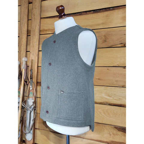 A unisex waistcoat made from recycled wool, displayed on a mannequin against a wooden background, featuring two patch pockets and natural shell buttons.