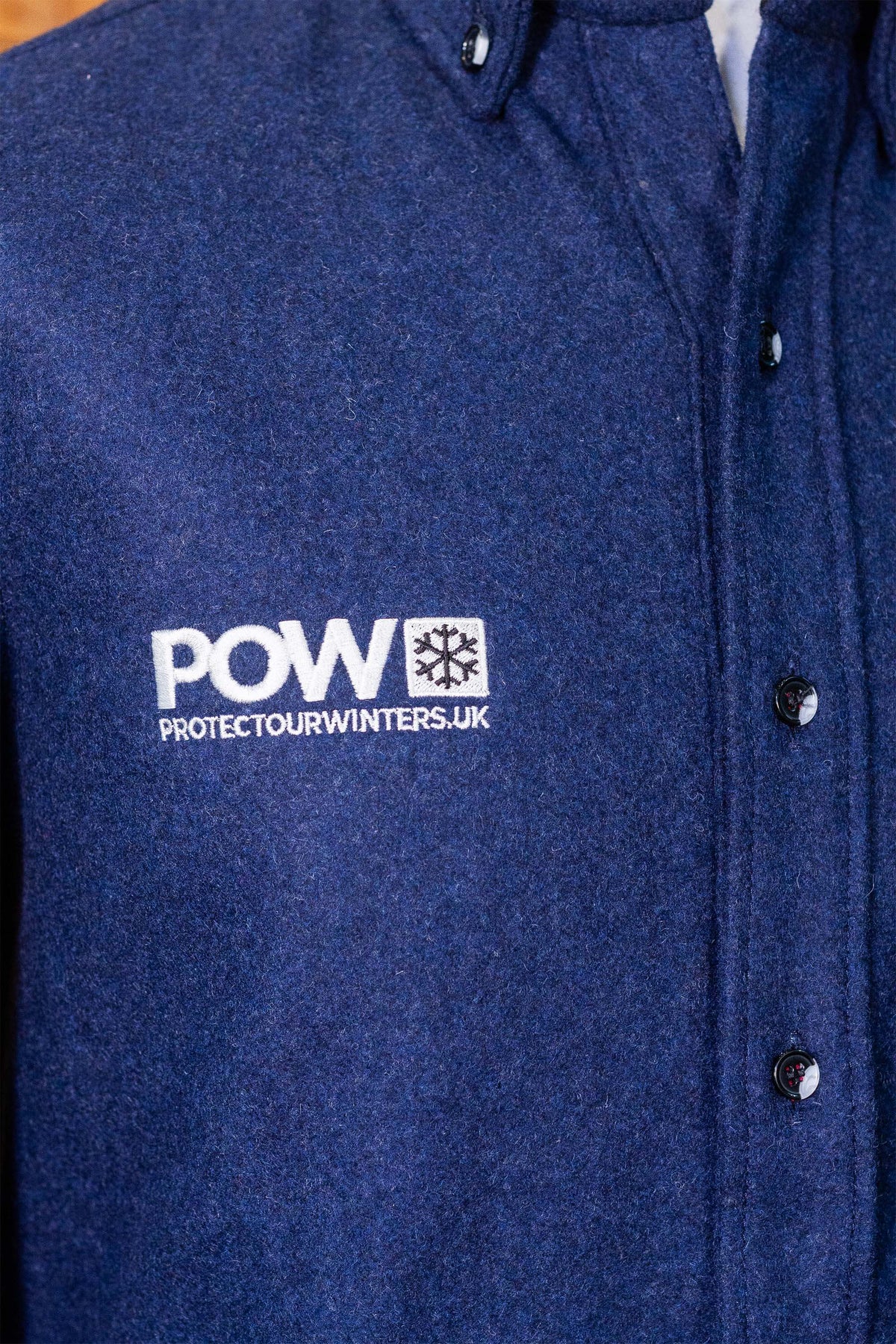 Close-up of the POW protectourwinters.uk embroidery and buttons on the chest