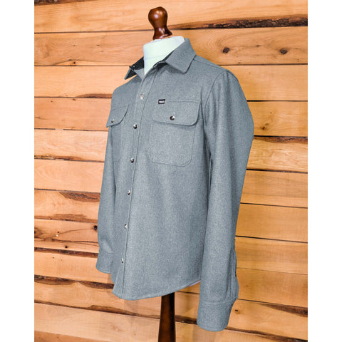 A men's long-sleeved shirt in a solid color, displayed on a mannequin against a wooden panel background. The shirt has two chest pockets with button-secure flaps and a button-down collar.